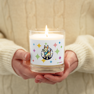 Candle with a colorful label featuring a dog illustration held by hands against a beige background